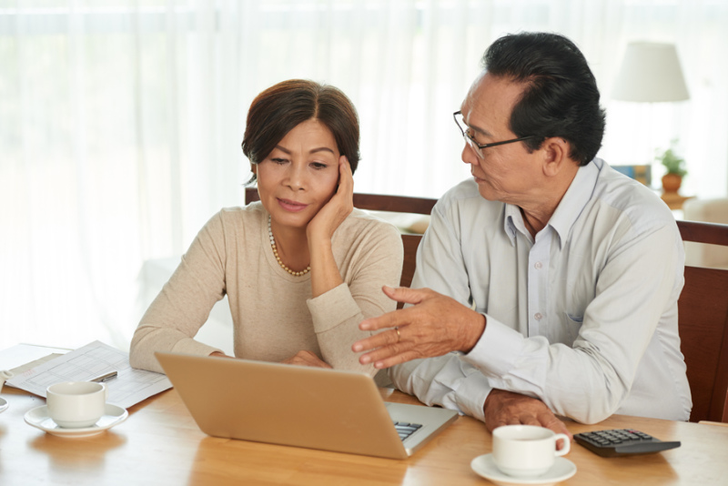Unhappy Vietnamese senior couple discussing family budget.