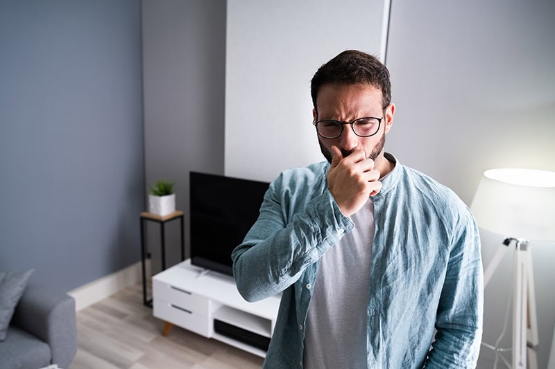 A man pinching his nose due to a bad odor in a modern living room.
