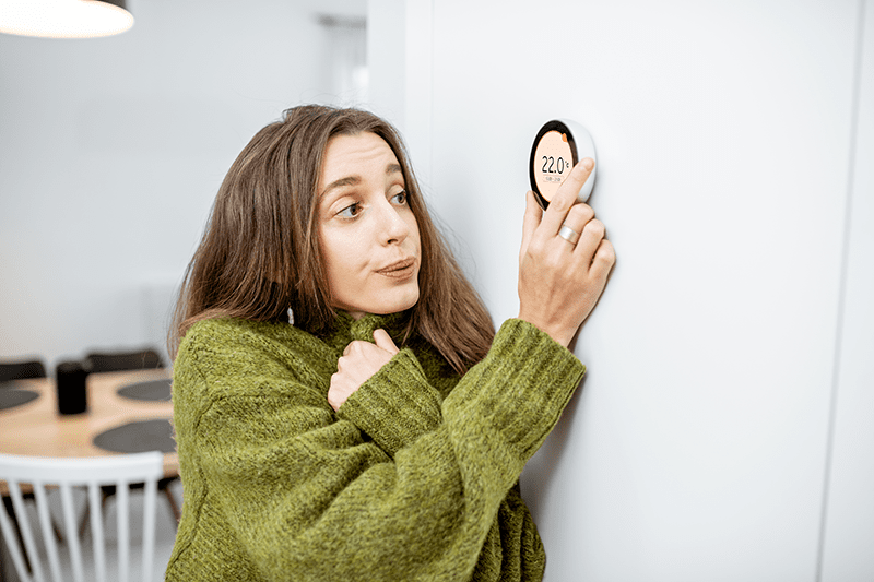 Woman adjusting thermostat, wondering why her heat pump keeps turning on and off. Ben’s Heating, AC & Electrical blog image.