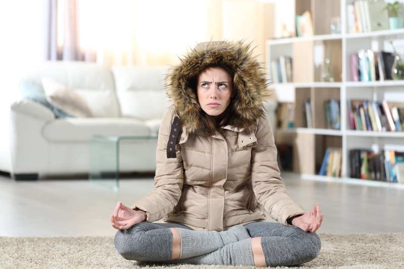 Woman trying to meditate, but can't concentrate due to being cold, because her heat pump is blowing out cold air.