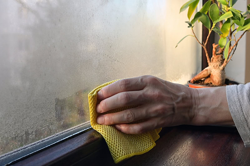 hand using a towel to wipe off indoor condensation from window.