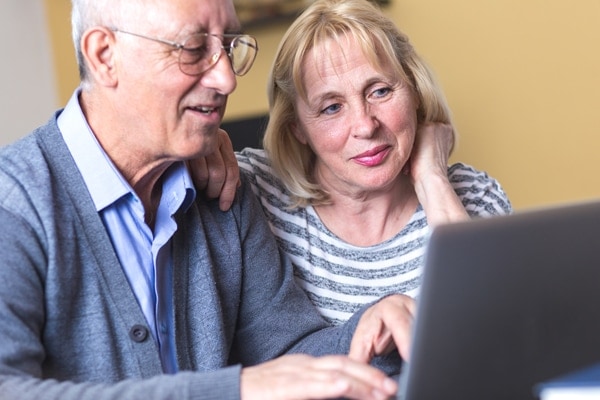 Happy senior couple using laptop at home to learn about heat pumps in Portland