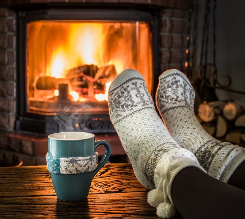 Warming and relaxing near fireplace. Woman feet near the cup of hot drink in front of fire.