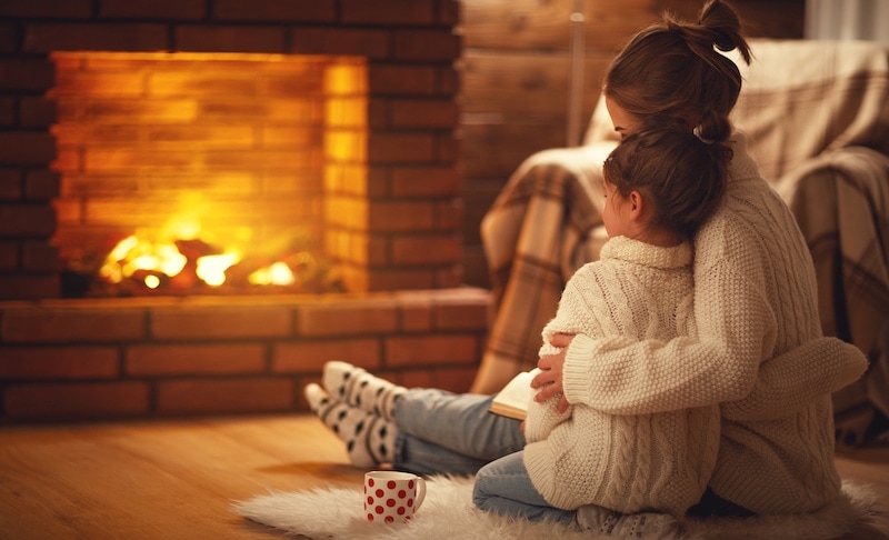 family mother and child daughter hugs and warm on winter evening by fireplace